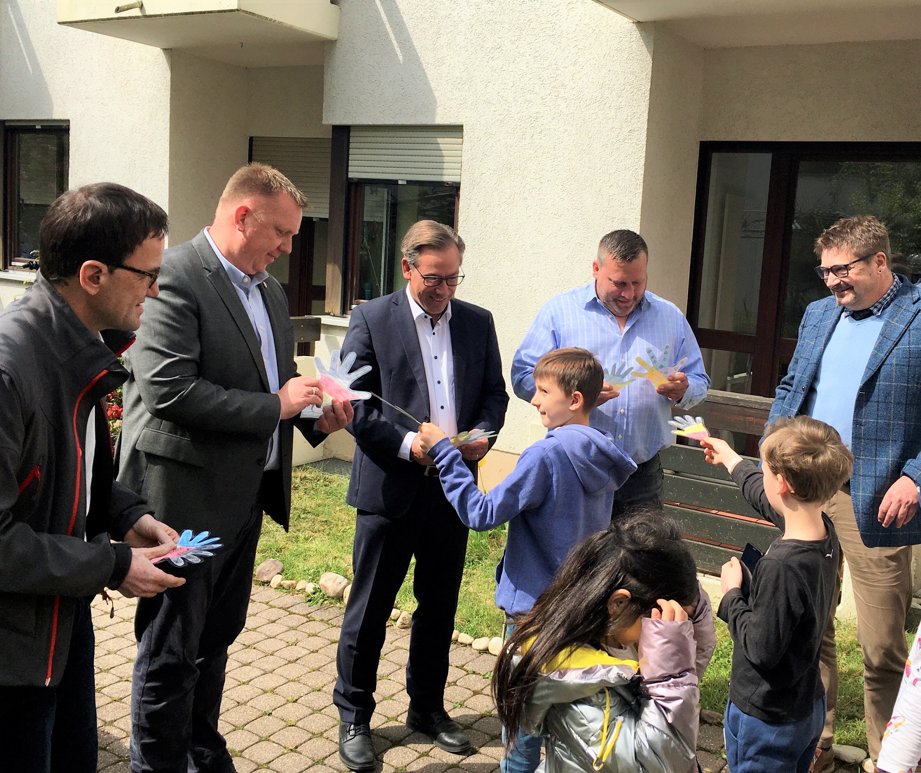 Gastgeschenke für Landrat Alexander Tritthart (Mitte), Bürgermeister Norbert Stumpf (2.v.l.), Diözesan-Caritasdirektor Michael Endres (links) und Einrichtungsleiter Benjamin Fricke (2.v.r.): Die Kinder der Notunterkunft in Bubenreuth haben ihre Hände auf Papier und Stoff gemalt, ausgeschnitten, laminiert und als „Dankeschön“ überreicht.