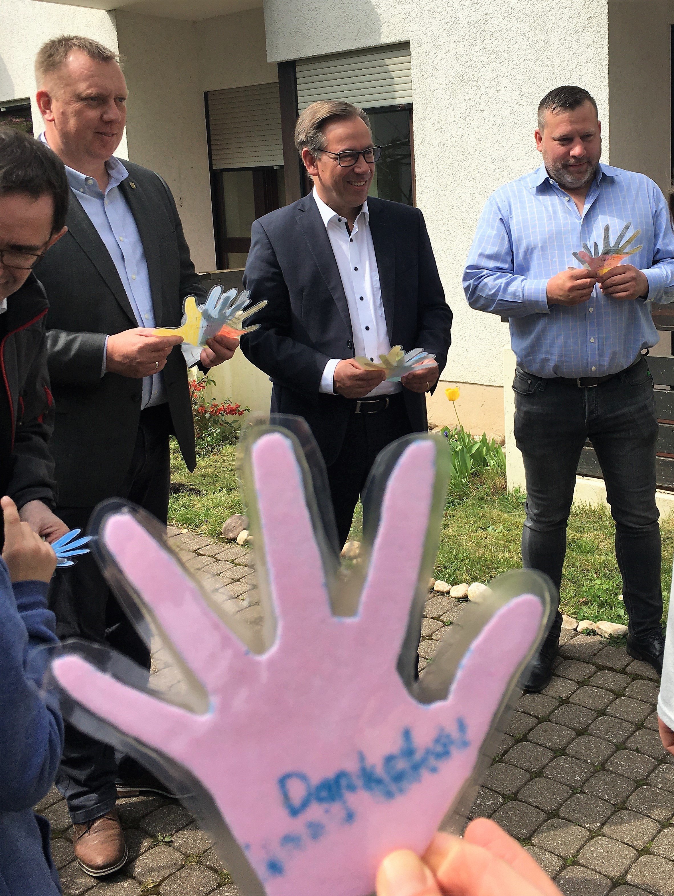 Gastgeschenke für Landrat Alexander Tritthart (Mitte), Bürgermeister Norbert Stumpf (2.v.l.), Diözesan-Caritasdirektor Michael Endres (links) und Einrichtungsleiter Benjamin Fricke (rechts): Die Kinder der Notunterkunft in Bubenreuth haben ihre Hände auf Papier und Stoff gemalt, ausgeschnitten, laminiert und als „Dankeschön“ überreicht.