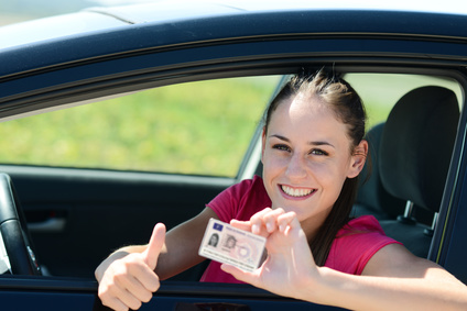 Lächelnde Frau im Auto mit Führerschein und "Daumen hoch"